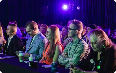 Audience seated in a Be Herd 2026 session under purple stage lighting