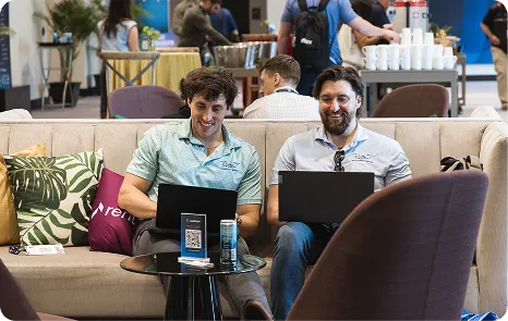 Two attendees working on laptops in a lounge at Be Herd 2026